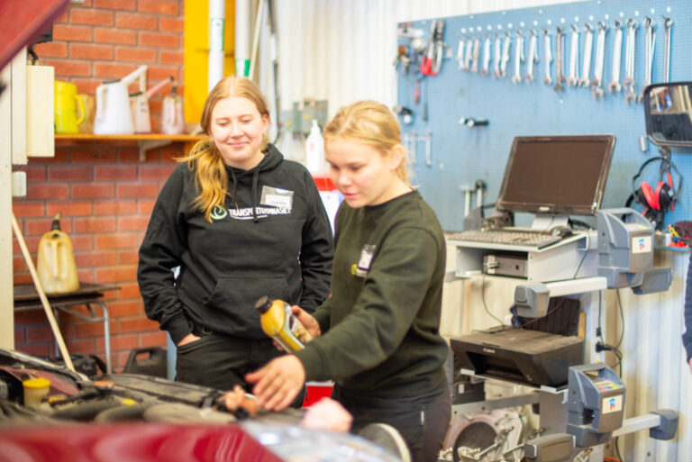 Elev på Transportgymnasiet byter olja under motorhuven på en bil.