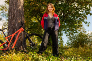 En elev på Äventyrsgymnasiet i Älvdalen står vid ett träd med en mountainbike.