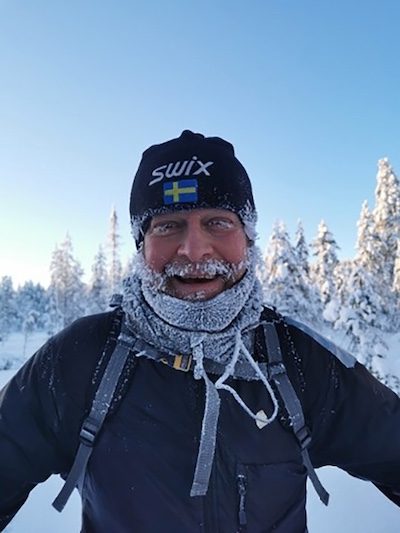 Wadman Erik Wadman - äventyrslärare som gillar skidåkning, står ute i ett snölandskap och skrattar med is i skägget.